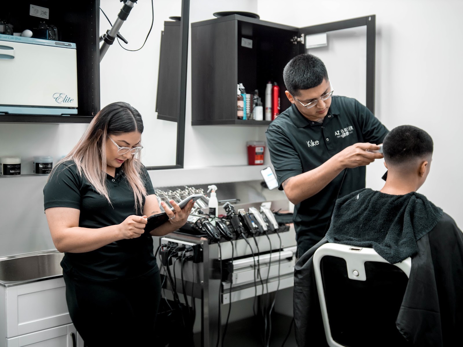 Kike dialing in a fade at his station, hot towel warmer and clipper rack behind him
